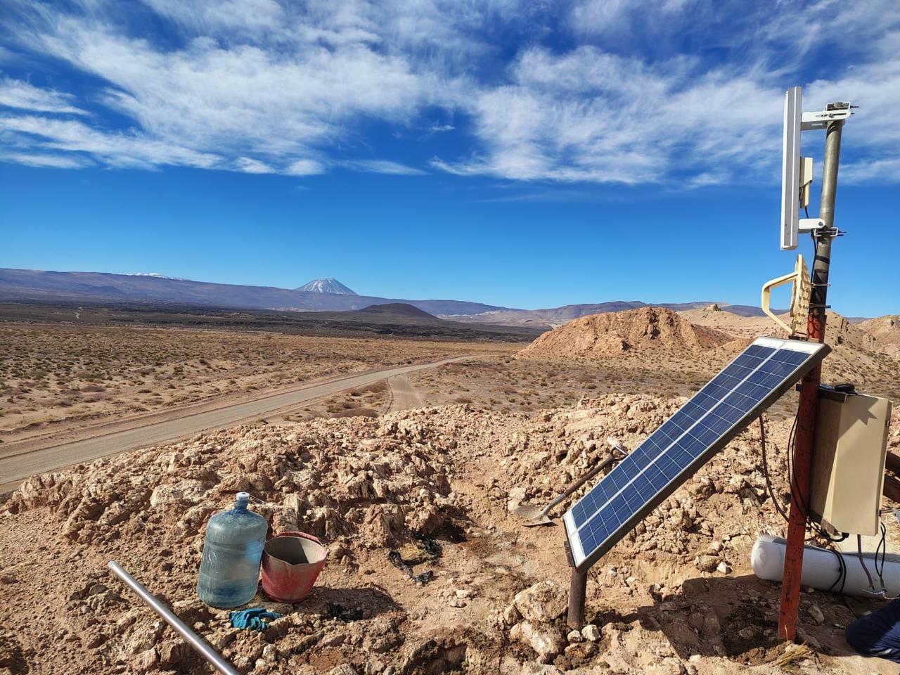Antena y panel solar en un sitio remoto con camino y volcán de fondo
